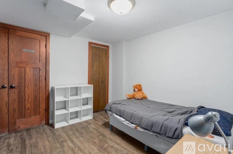 A bedroom with a bed, a teddy bear, and a white shelf.
