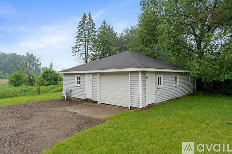 A white house with a grey roof is surrounded by greenery.