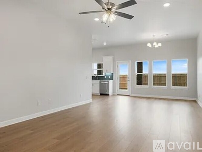 A spacious room with a ceiling fan and a kitchen area in the background.