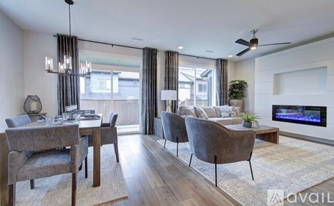 A living room with a grey sofa, a wooden dining table with grey chairs, a white rug, a television, and a ceiling fan.