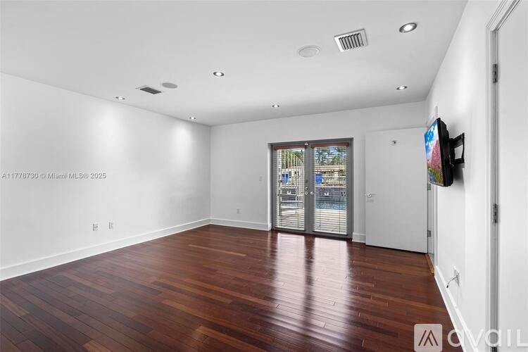 A spacious room with wood flooring and a large window.