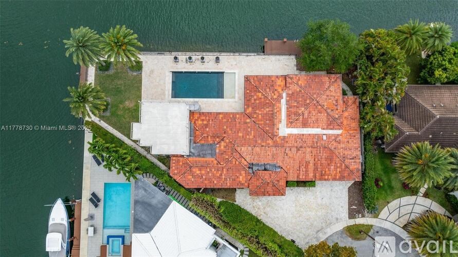 A house with a red roof is surrounded by greenery and a body of water.