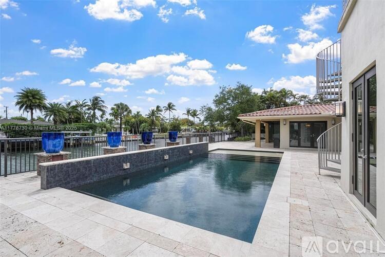 A pool surrounded by a stone patio and a house with a balcony.
