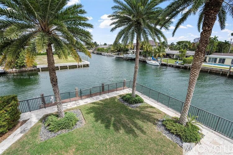A view of a waterfront with palm trees and a fence.