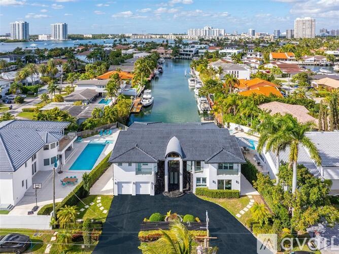 A large white house with a black roof and a pool in the front yard.
