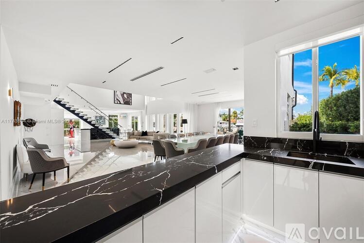 A modern kitchen with a marble countertop and a view of a palm tree outside the window.