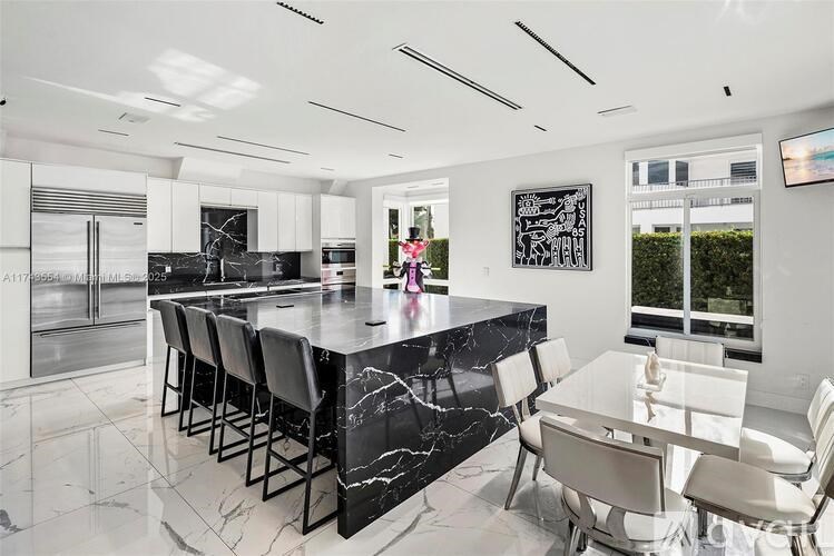 A modern kitchen with a black marble island and white chairs.
