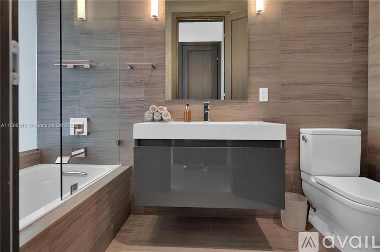 A modern bathroom with a large mirror, a bathtub, and a toilet.