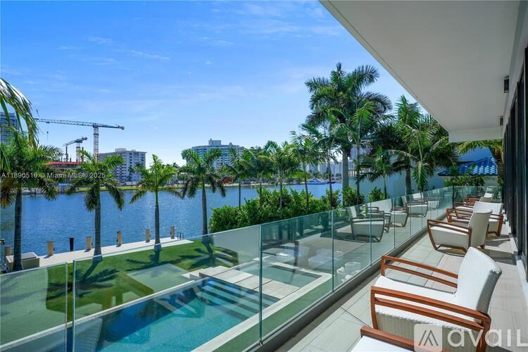 A glass balcony with chairs overlooking a body of water and palm trees.