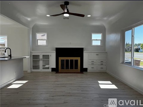 A spacious room with a fireplace, ceiling fan, and large windows.