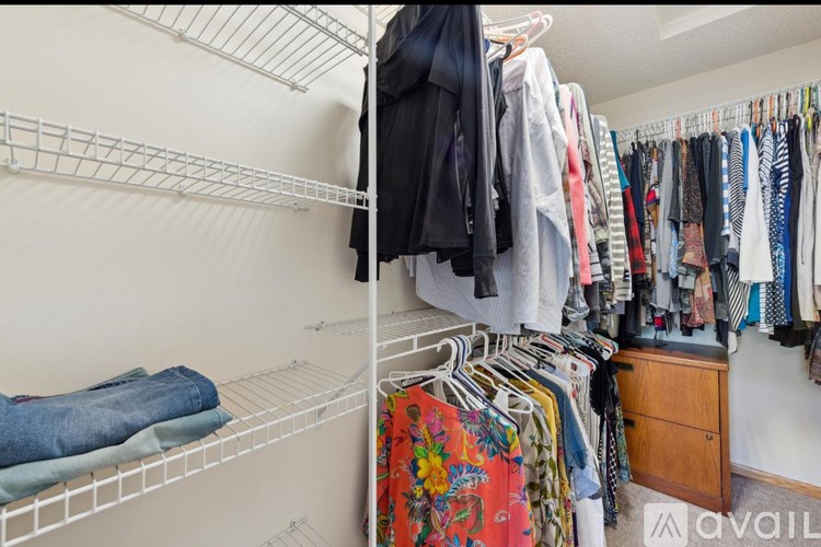 A white closet with clothes hanging and folded on shelves.