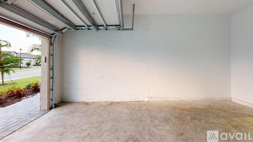 A spacious garage with a white wall and a door open to a driveway.