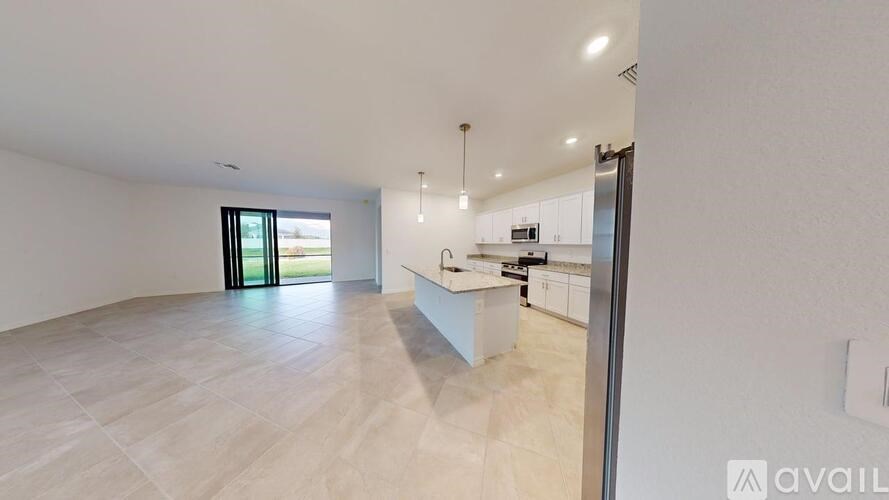 A spacious room with a kitchen area and a sliding glass door leading to a balcony.