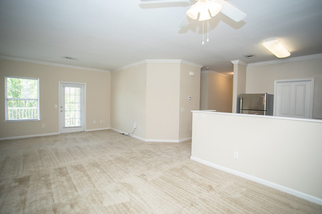 an empty living room with a kitchen and a ceiling fan