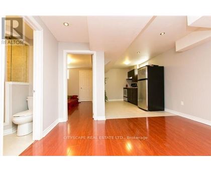 A spacious room with a wooden floor and a black refrigerator.