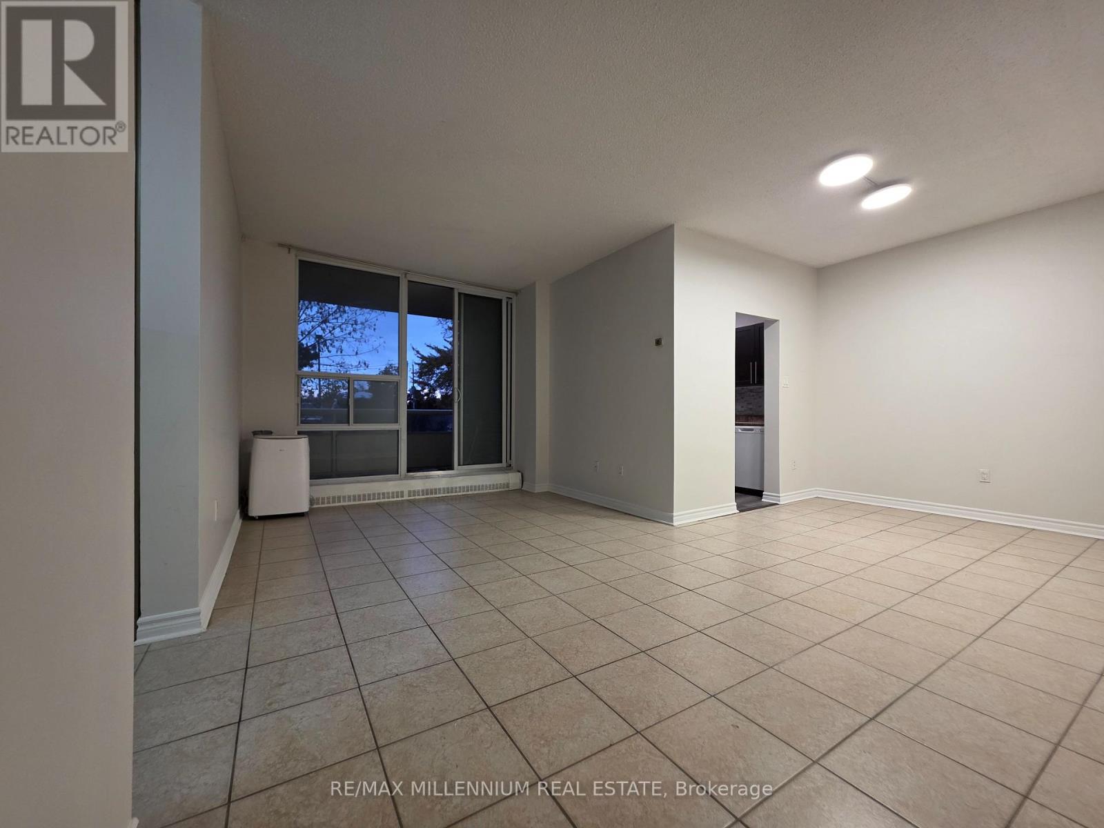 A spacious room with tiled flooring and a sliding glass door leading to a balcony.