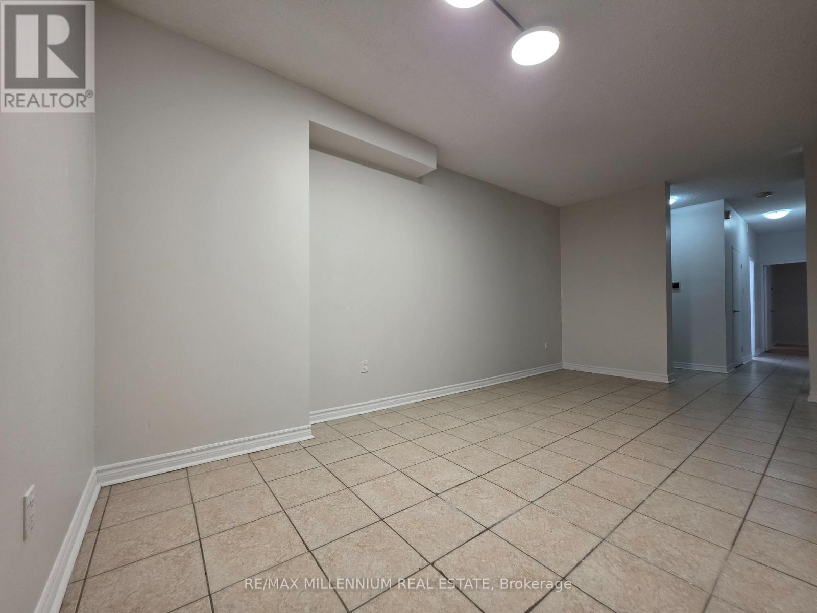 A spacious room with beige tiled flooring and white walls, featuring a large window and a doorway leading to another room.