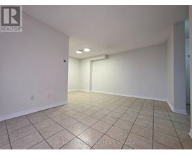 A spacious room with beige tiled flooring and white walls, featuring a large window and a doorway leading to another room.