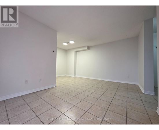 A spacious room with beige tiled flooring and white walls, featuring a large window and a doorway leading to another room.