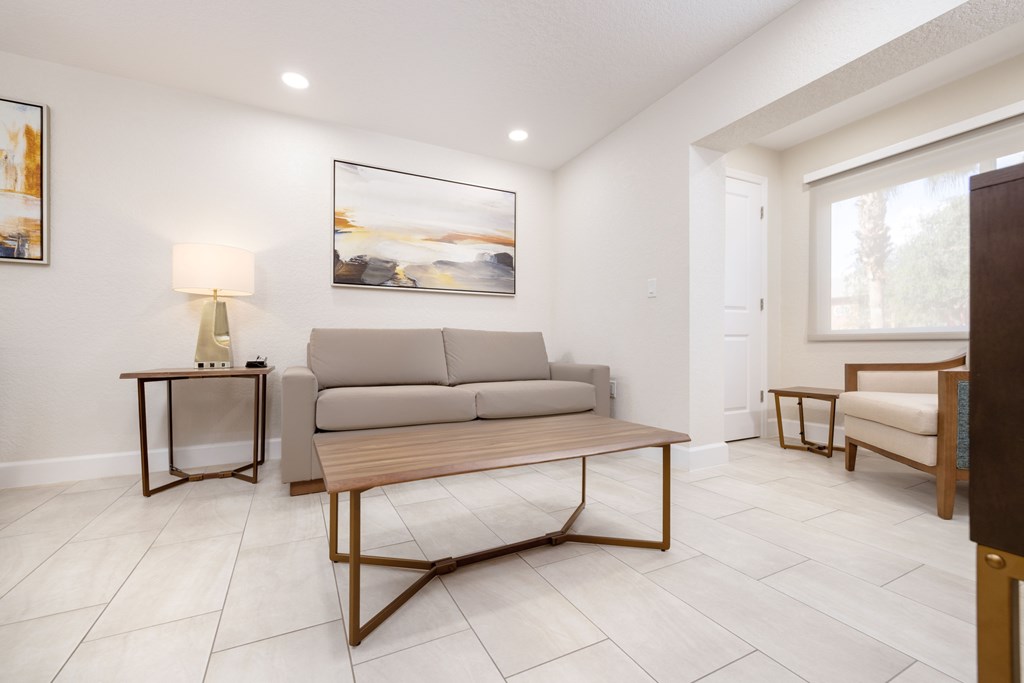 A living room with a grey couch, a wooden table, and a painting on the wall.
