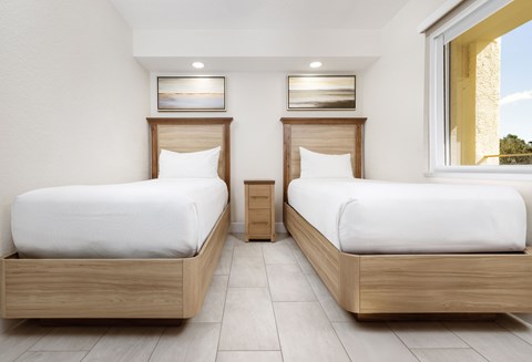 Two beds in a room with white bedspreads and wooden headboards.