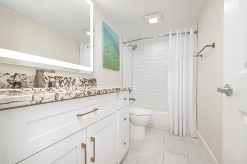 A white bathroom with a marble counter top and a shower with a white curtain.