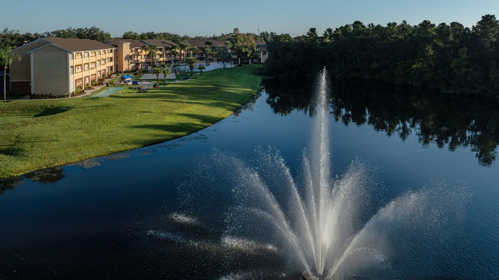 A fountain in the middle of a lake in front of a building.