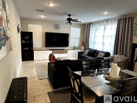 A woman is sitting on a black couch in a living room with a television and a fan.