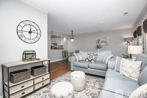 A living room with a grey couch, a white ottoman, and a wooden cabinet with baskets on top.