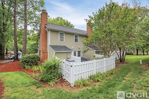 A house with a white fence and green trees in front.