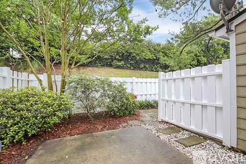 A white fence borders a yard with a gravel path and green shrubbery.
