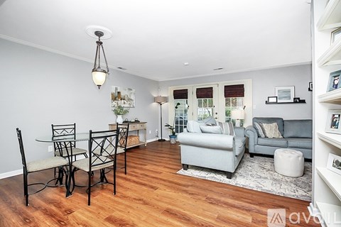 A living room with a grey couch, a white ottoman, and a wooden floor.