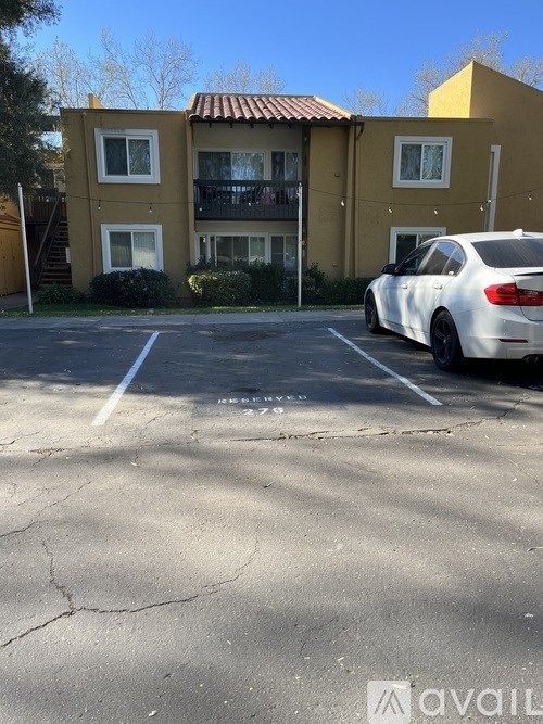 A white car is parked in a parking lot in front of a yellow building.