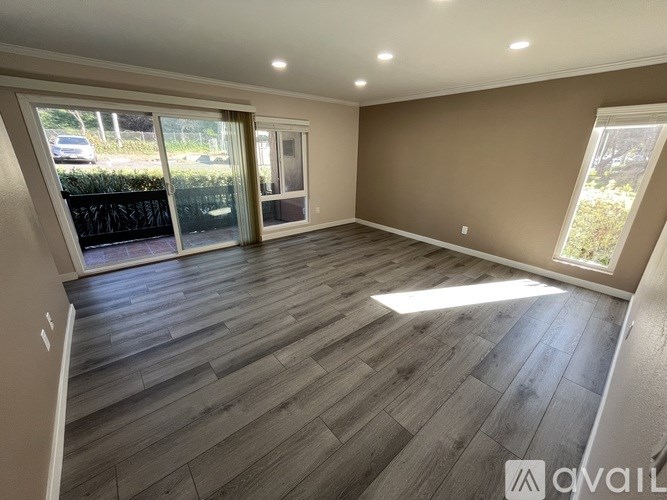 A spacious room with wooden flooring and large windows.