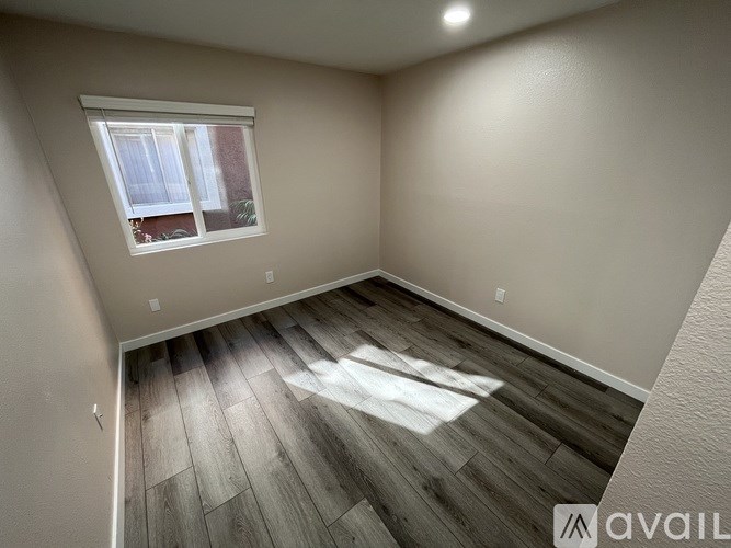 A room with wooden flooring and a window letting in sunlight.
