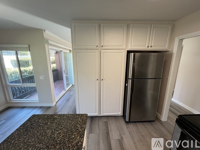 A kitchen area with a refrigerator, cabinets, and a patterned rug.
