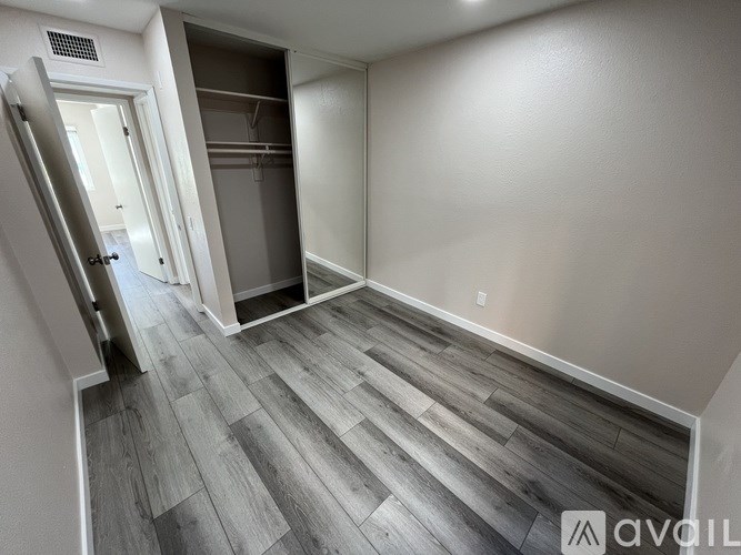 A room with a wooden floor and a white wall with a door open to another room.