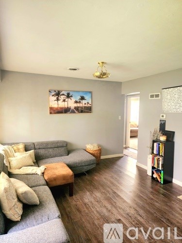 A living room with a grey couch and a painting of a beach scene on the wall.