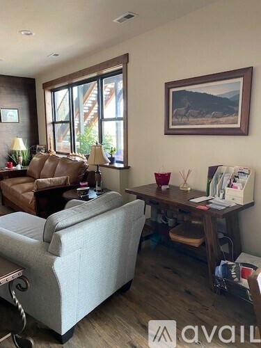 A living room with a grey couch, a brown leather chair, a wooden desk with a lamp, and a framed picture on the wall.