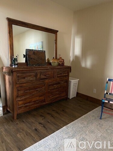 A wooden chest of drawers with a mirror on top is in a room with wooden flooring.