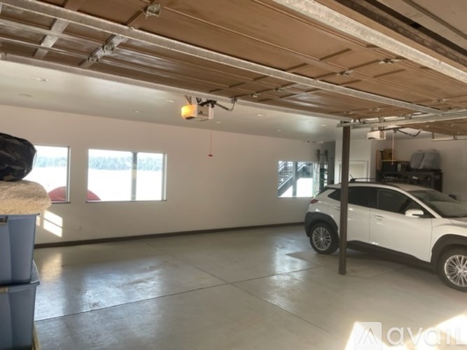 A white car is parked in a large, empty garage with a wooden ceiling and a window.