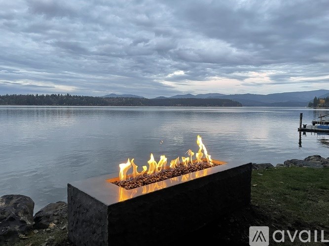 A modern fire pit with flames burning in front of a lake.