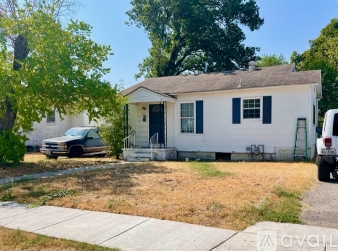 A white house with black shutters is in front of a tree and a parked van.