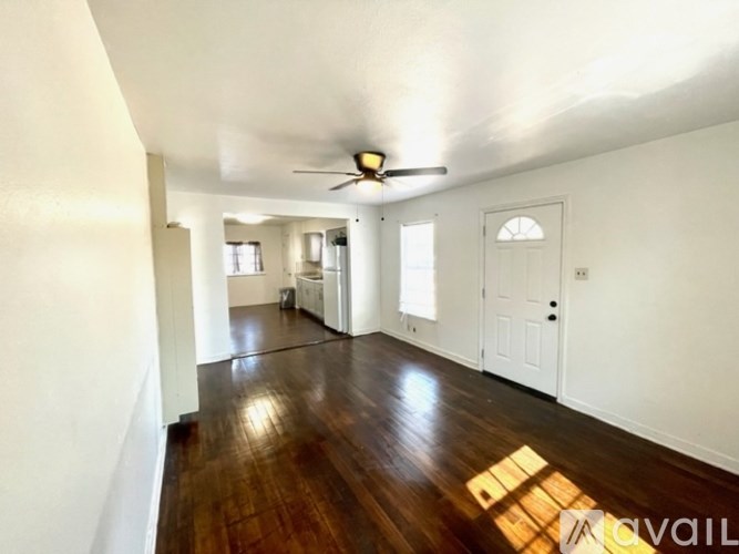A room with wooden floors and white walls, a ceiling fan, and a door.