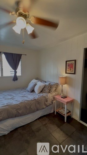 A bedroom with a bed, a small table with a lamp, and a ceiling fan.