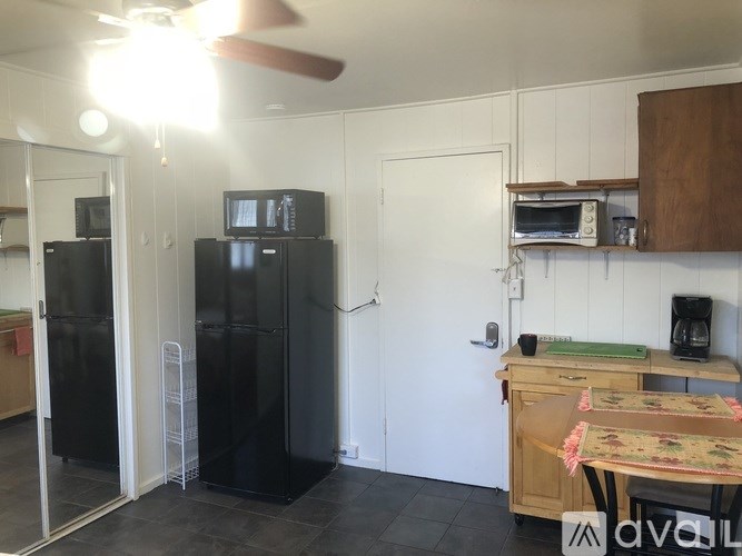 A kitchen with a black fridge, a fan, and a table with a floral tablecloth.