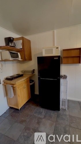 A kitchen with a black fridge, wooden cabinets, and a microwave.