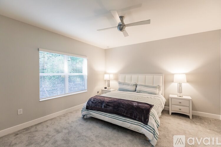 A bedroom with a large bed, two lamps, and a ceiling fan.