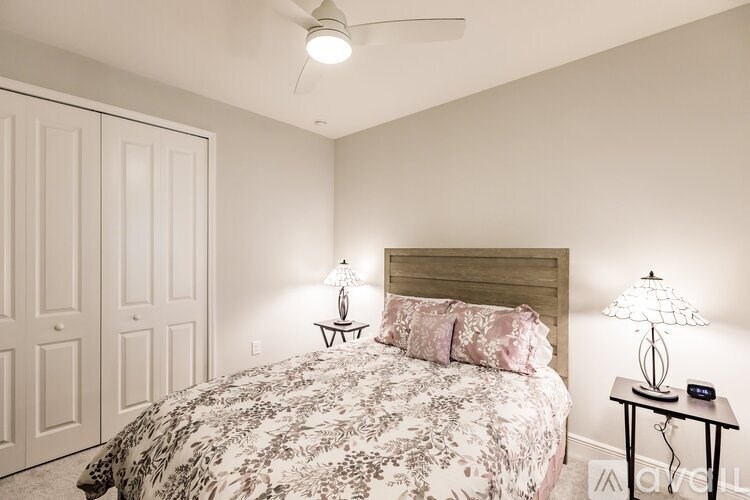 A bedroom with a bed, two lamps, and a ceiling fan.