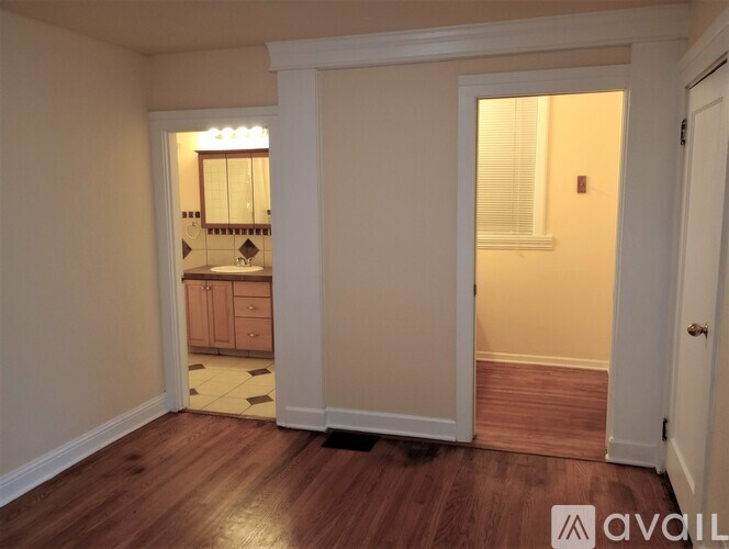 A room with wooden floors and a kitchen area in the background.